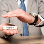 cropped view of businessman covering wooden block with word copyright with hand isolated on grey